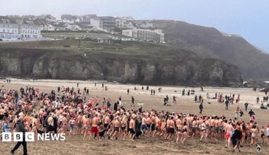 A group of many people on a beach, running towards the sea in swimwear.