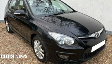 A black Hyundai i30 car with the registration plate blurred out  is parked on light-coloured gravel.