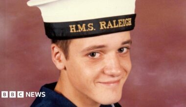 Simon Parkes smiles at the camera in a portrait photo. He wears a navy uniform with an HMS Raleigh cap