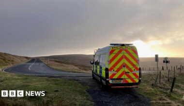 A police van parked on a path of a bending road. The sun is setting over the hills in the distance.