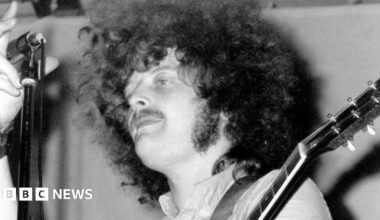 Mick Abrahams grabbing a microphone while playing guitar at a gig.