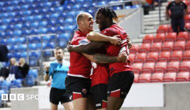 Three Salford Red Devils players celebrate scoring a try during a match in 2025