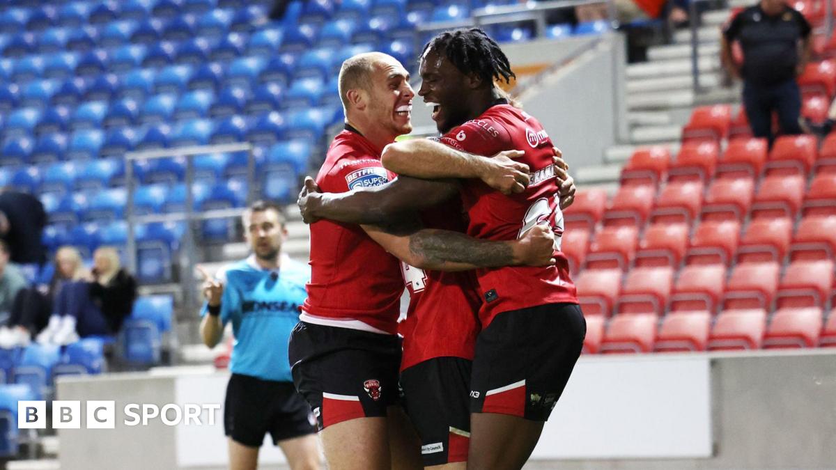 Three Salford Red Devils players celebrate scoring a try during a match in 2025