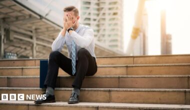 A man in office clothes sits on some steps. He looks bereft of hope.
