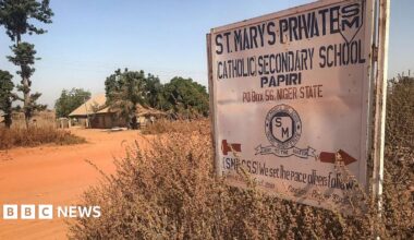 A sign that reads St. Mary's Private Catholic Secondary School Papiri, Niger State, is positioned on the right with red dirt road and a building in the background surrounded by trees.