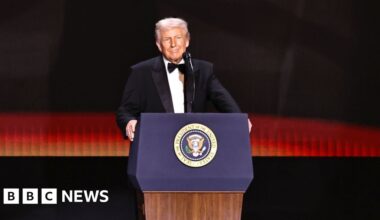Trump in a suit and tie, stands on stage before a POTUS lectern.
