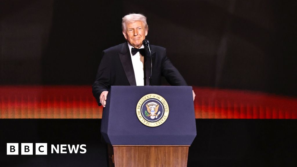 Trump in a suit and tie, stands on stage before a POTUS lectern.