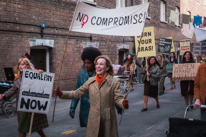 Laura Main as Shelagh Turner in Call the Midwife, marching down the street with other women, holding a sign that reads 'NO COMPROMISE'.