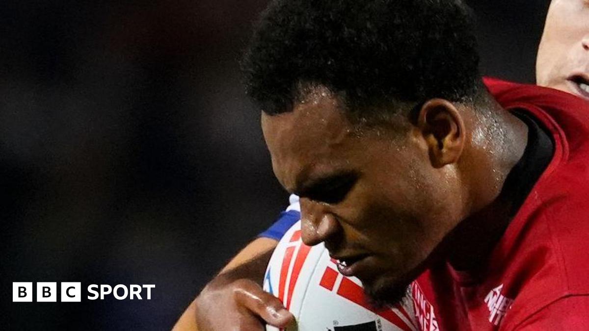 Leon Ruan, holding the ball under his right arm, being tackled by a Wakefield player in a game for Salford