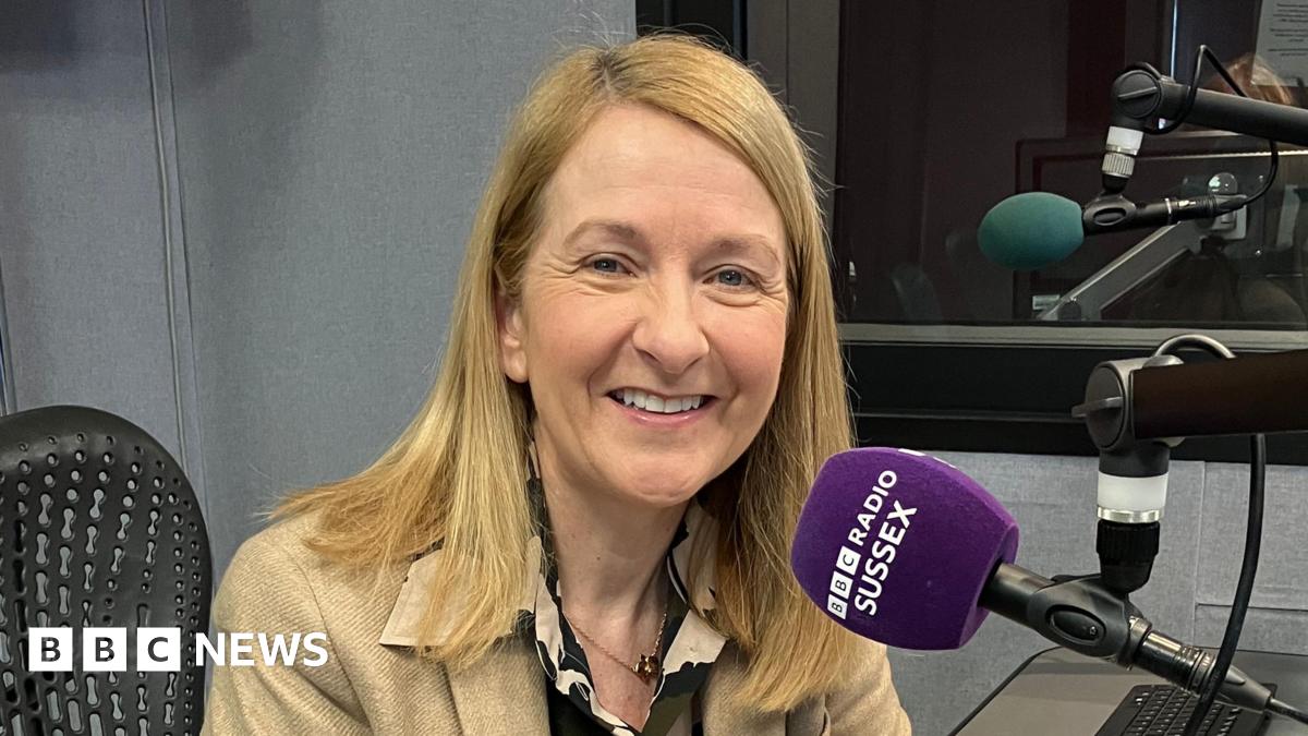 Katy Bourne sitting in a recording booth in front of a purple microphone which has "BBC RADIO SUSSEX" on it.