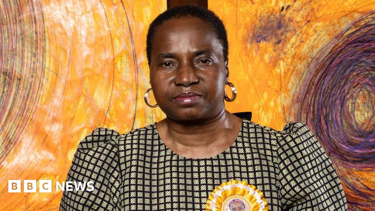 A brown NC500 sign post which says it is 27 miles to Ullapool next to a country road with hills in the background.