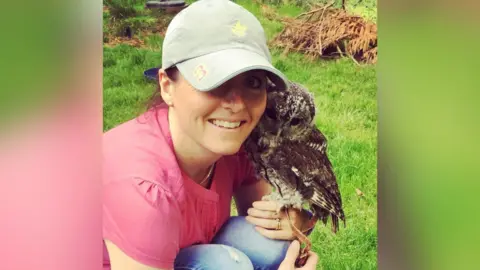 Caroline Beresford Caroline wearing a mint green cap and a pink shirt. She is crouched for the camera with a barn owl on her left arm.