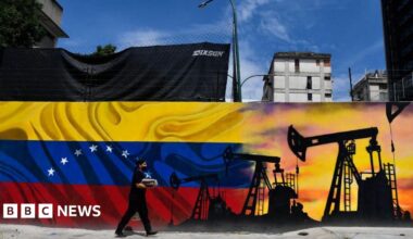 A man wearing a face masks walks past a mural depicting an oil pump and the Venezuelan flag in a street of Caracas, on May 26, 2022. (Photo by Federico PARRA / AFP)