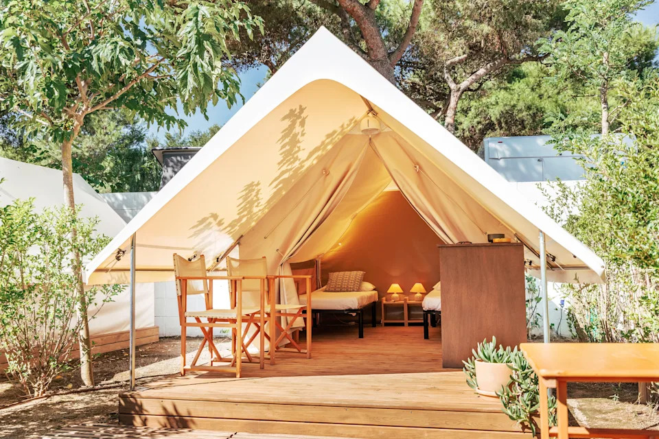 Luxurious glamping tent setup with chairs and a bed, nestled among greenery, suggesting a blend of comfort and nature for a travel article