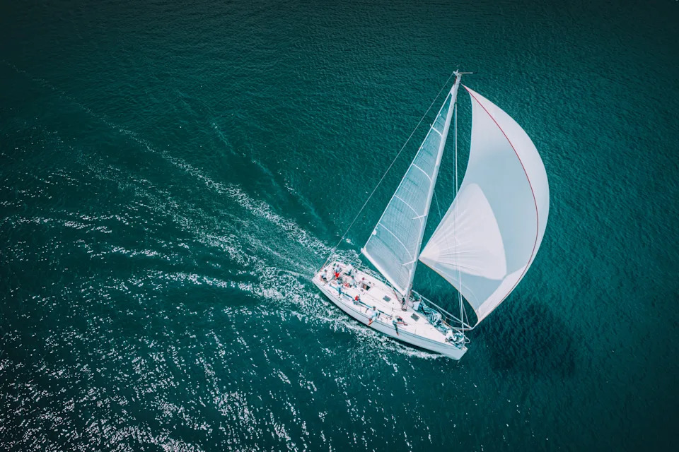 Aerial view of a sailboat gliding across the ocean, showcasing leisure or potential luxury context in the Work & Money category