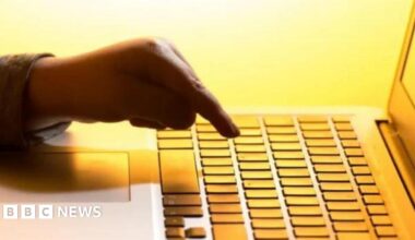 A man with a grey sleeve holds his finger over a button on a laptop.