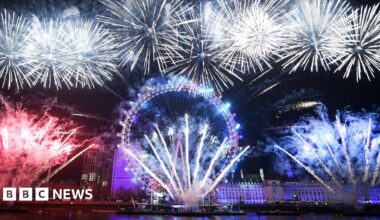 A woman walks a dog during sunrise on Primrose Hill. A silhoutte of the city is in the background amongst a cloudy yellow sly.