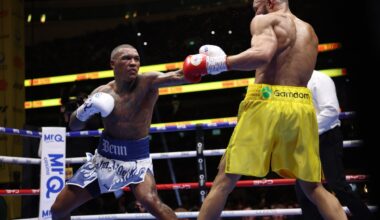 Conor Benn extends a left hand toward Chris Eubank Jr. during their rematch, with Benn in blue-and-white trunks and Eubank Jr. in yellow, inside the ring at Tottenham Hotspur Stadium in London.