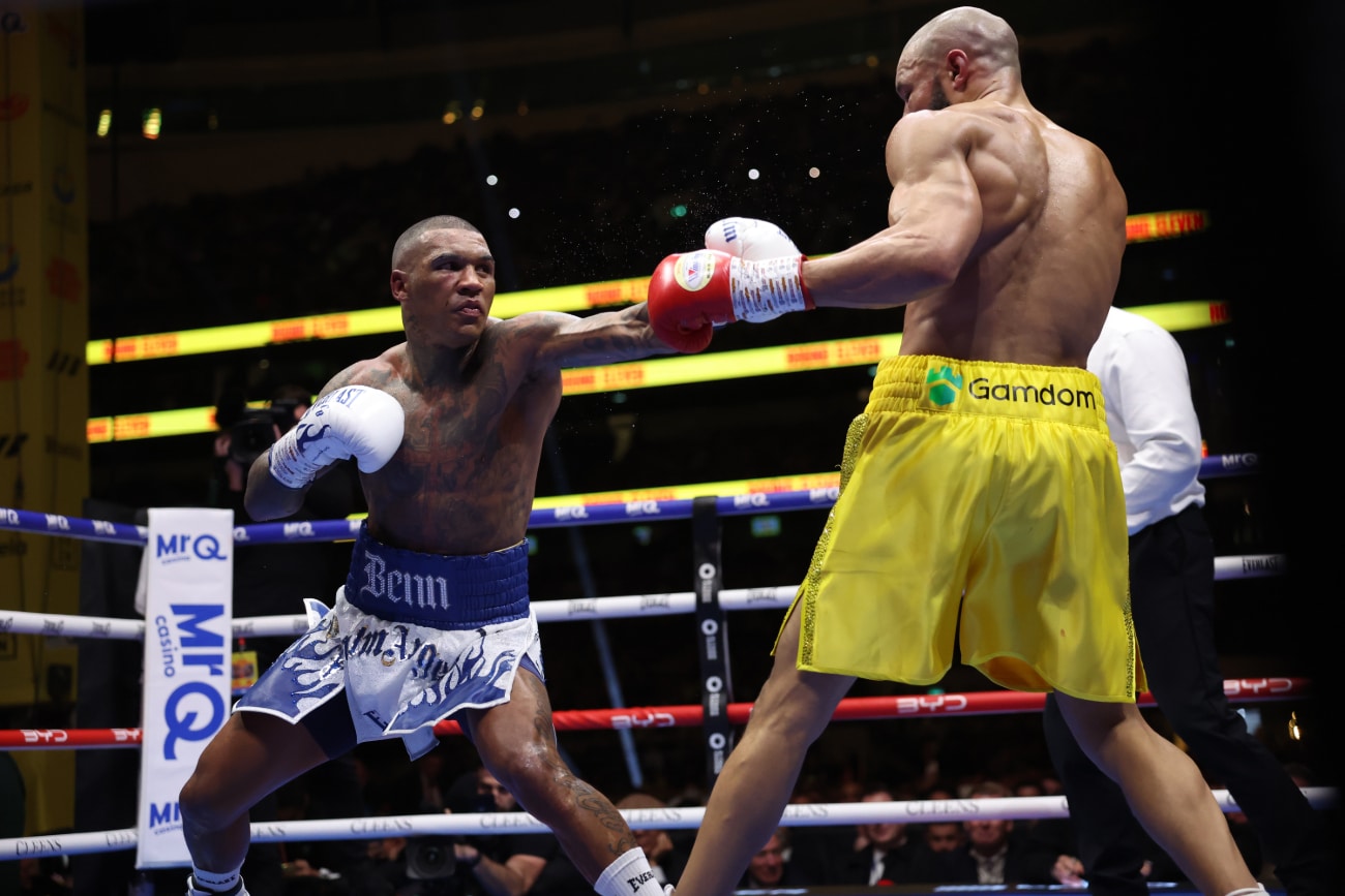 Conor Benn extends a left hand toward Chris Eubank Jr. during their rematch, with Benn in blue-and-white trunks and Eubank Jr. in yellow, inside the ring at Tottenham Hotspur Stadium in London.