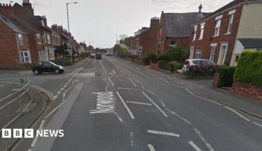 A view of a road. A black car is pulling out at a junction up ahead on the left and there are rows of houses either side of the road.