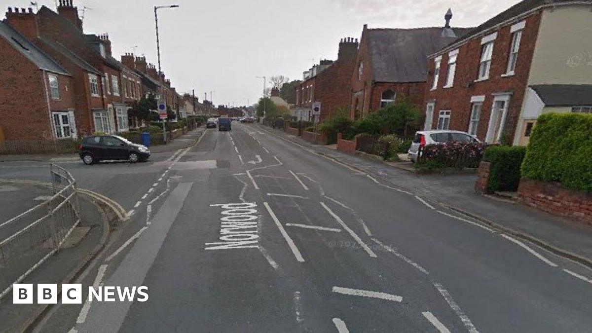 A view of a road. A black car is pulling out at a junction up ahead on the left and there are rows of houses either side of the road.