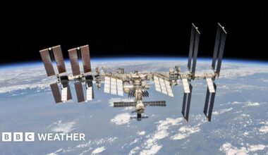 Snowy scene with a park area and a church in the background.  Trees covered in snow and a group of people walking in the snow.
