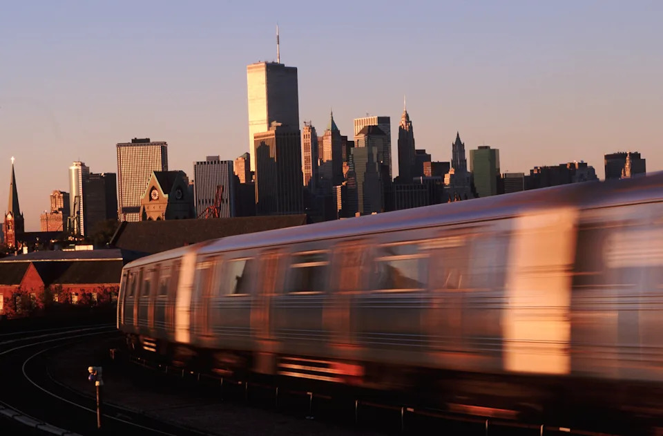 A fast-moving subway train in the foreground with a city skyline in the background, suggesting urban commuting