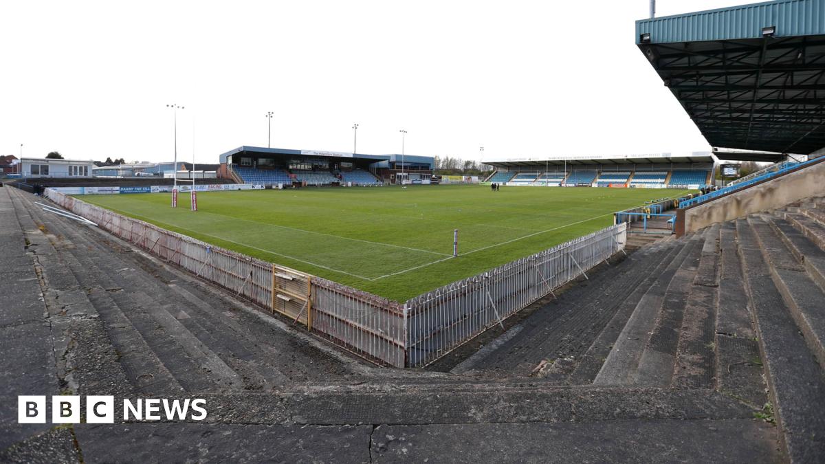 A brown NC500 sign post which says it is 27 miles to Ullapool next to a country road with hills in the background.
