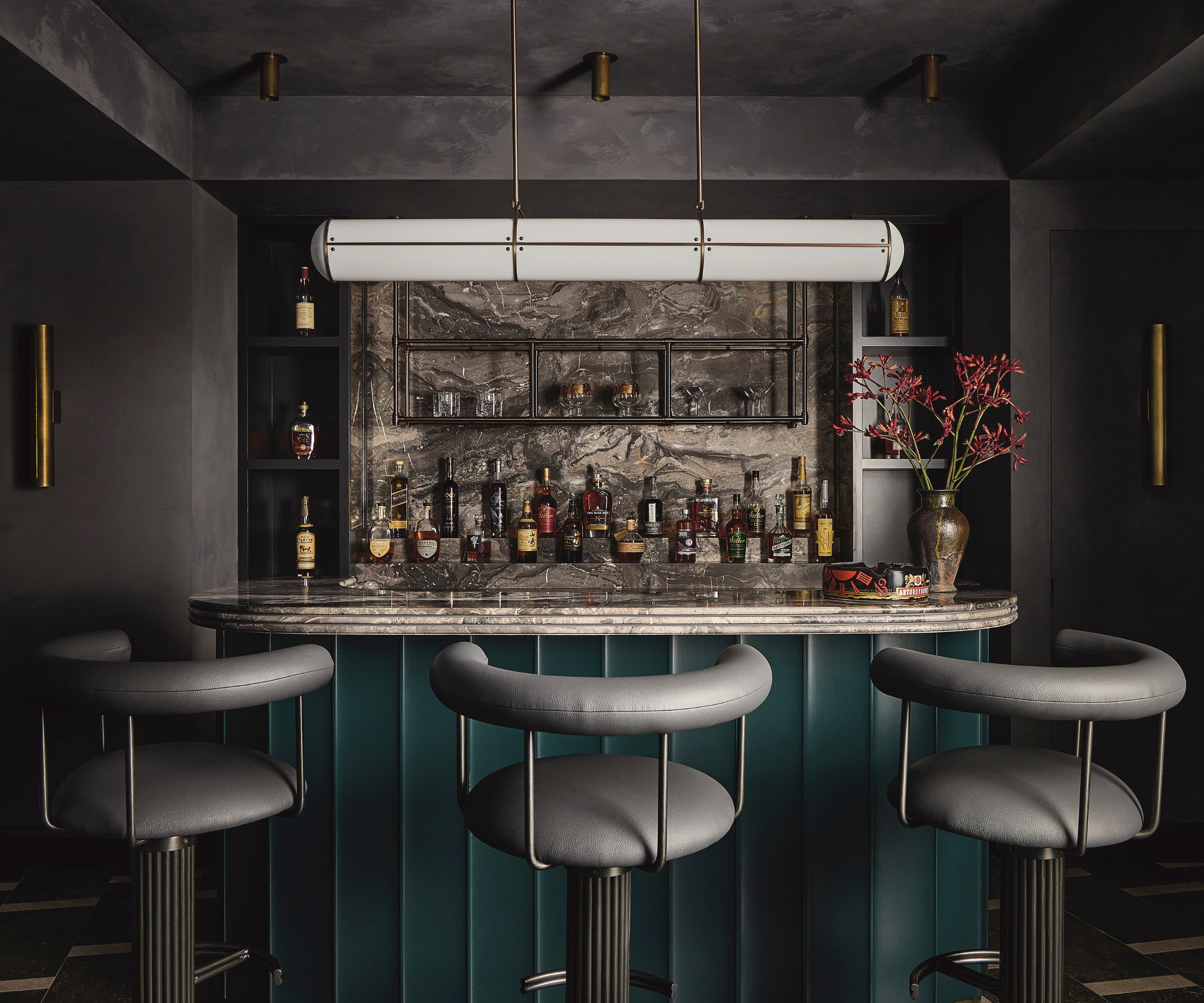 A moody bar with dark roman clay walls and gray-leather bar stools.