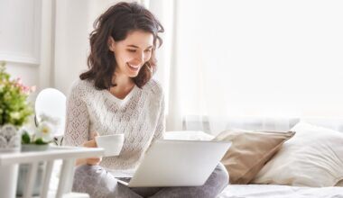 Happy woman sitting on a bed with a coffee and a Windows 11 laptop