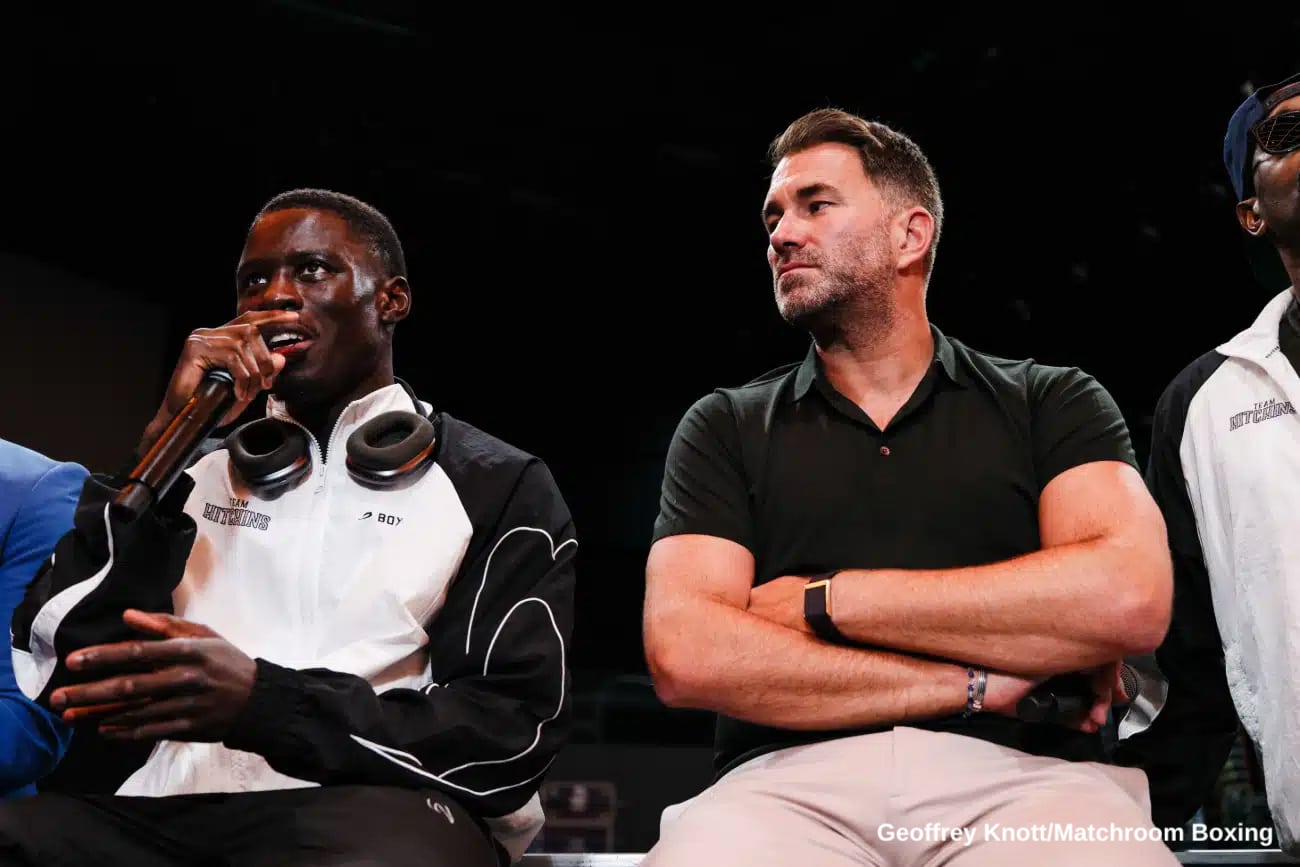 Richardson Hitchins speaks into a microphone during a press event while promoter Eddie Hearn sits beside him with folded arms, listening.