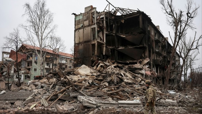 A Ukrainian police officer in camouflage gear walks past the rubble of heavily damaged buildings in Dobropillia.