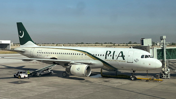 A Pakistan International Airlines passenger plane is parked at a gate, with ground crew working nearby at Islamabad International Airport.