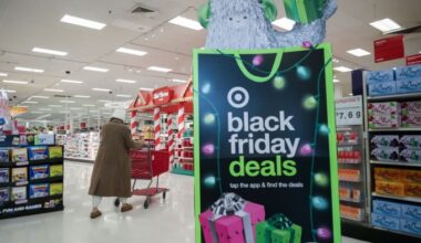 A large Black Friday deals sign with holiday lights and gift boxes stands near the entrance of a Target store as a shopper pushes a red cart.