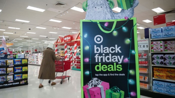 A large Black Friday deals sign with holiday lights and gift boxes stands near the entrance of a Target store as a shopper pushes a red cart.