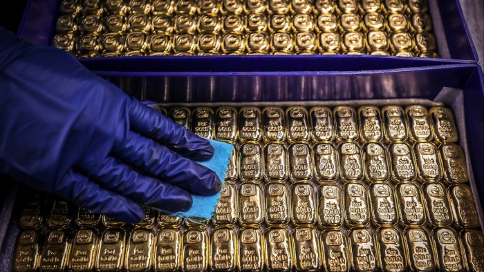 A worker wearing blue gloves polishes rows of gold bullion bars at the ABC Refinery.