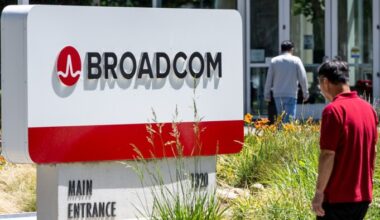 Broadcom headquarters sign with logo and text, with two people walking nearby and office doors in the background.