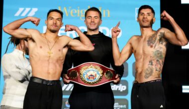 Two light welterweight fighters flex on the scale during an official weigh-in as an official stands between them holding a championship belt.