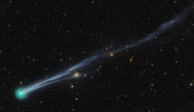 A bright green comet is pictured to the bottom left of a starfield against a black sky, with a long tail extending to the upper right of the screen.