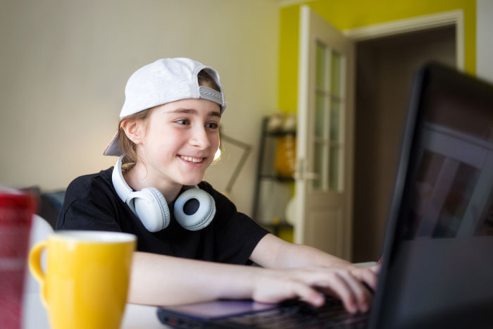 Young person wearing headphones and a backward cap, smiling while using a laptop, exploring AI industry insights at home.