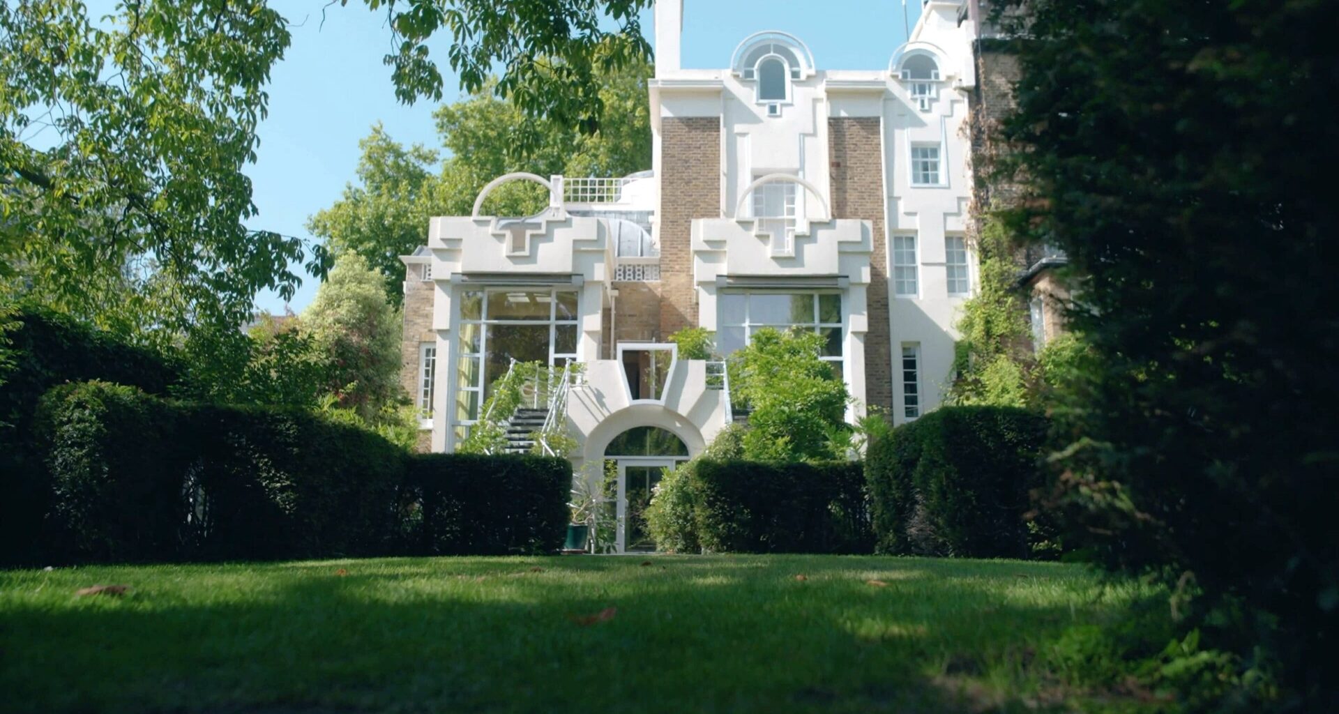 Front view of The Cosmic House in west London, framed by trees and manicured gardens