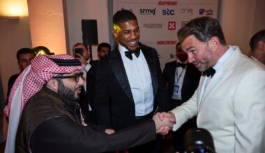 Turki Alalshikh shakes hands with promoter Eddie Hearn during a boxing industry event, as Anthony Joshua looks on in the background.