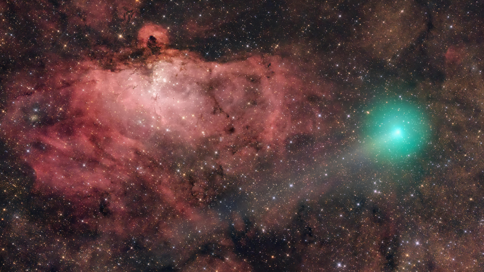 A green comet can be seen glowing to the right of a deep-space image, with a faint tail extending to the lower left. A swirling red nebula can be seen dominating the background to the left of the screen, with a number of particularly bright stars clustered below a dense horizontal filament of cosmic dust.