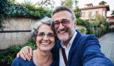 A couple wearing blue is outdoors, smiling for a selfie.