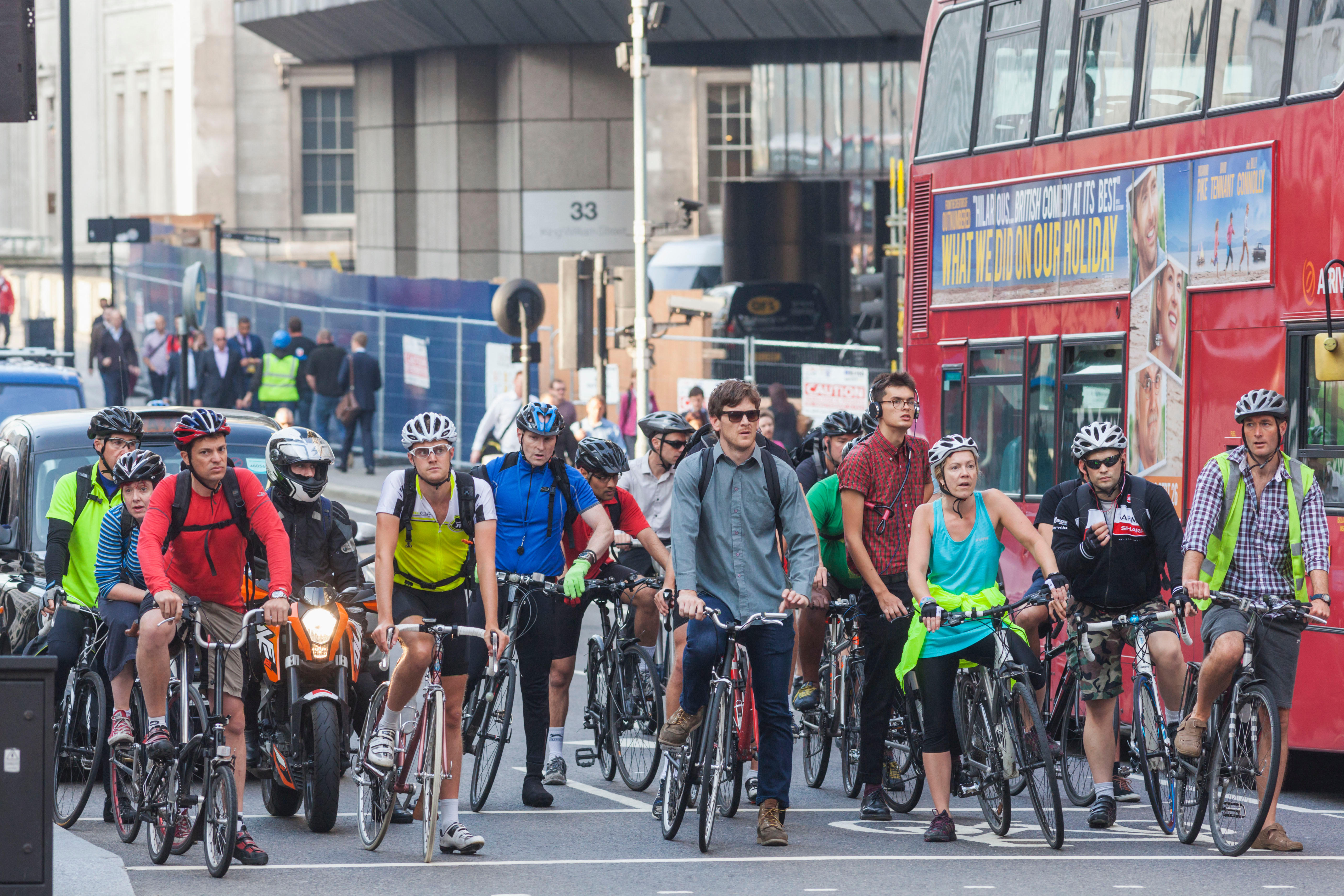 A group of cyclists, including a red double-decker bus, stopped at a traffic light in London.
