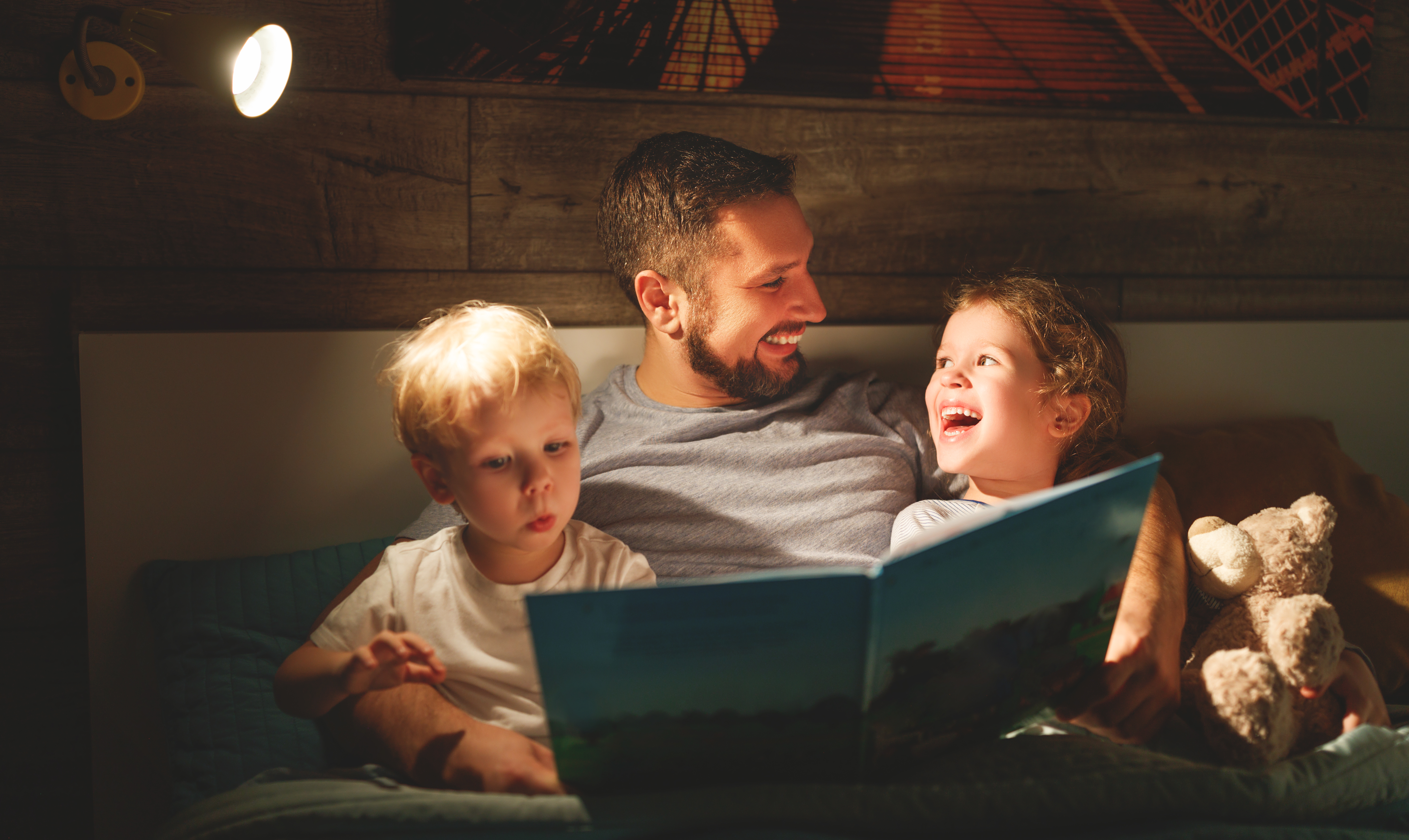 A father reading a book to his two young children in bed.