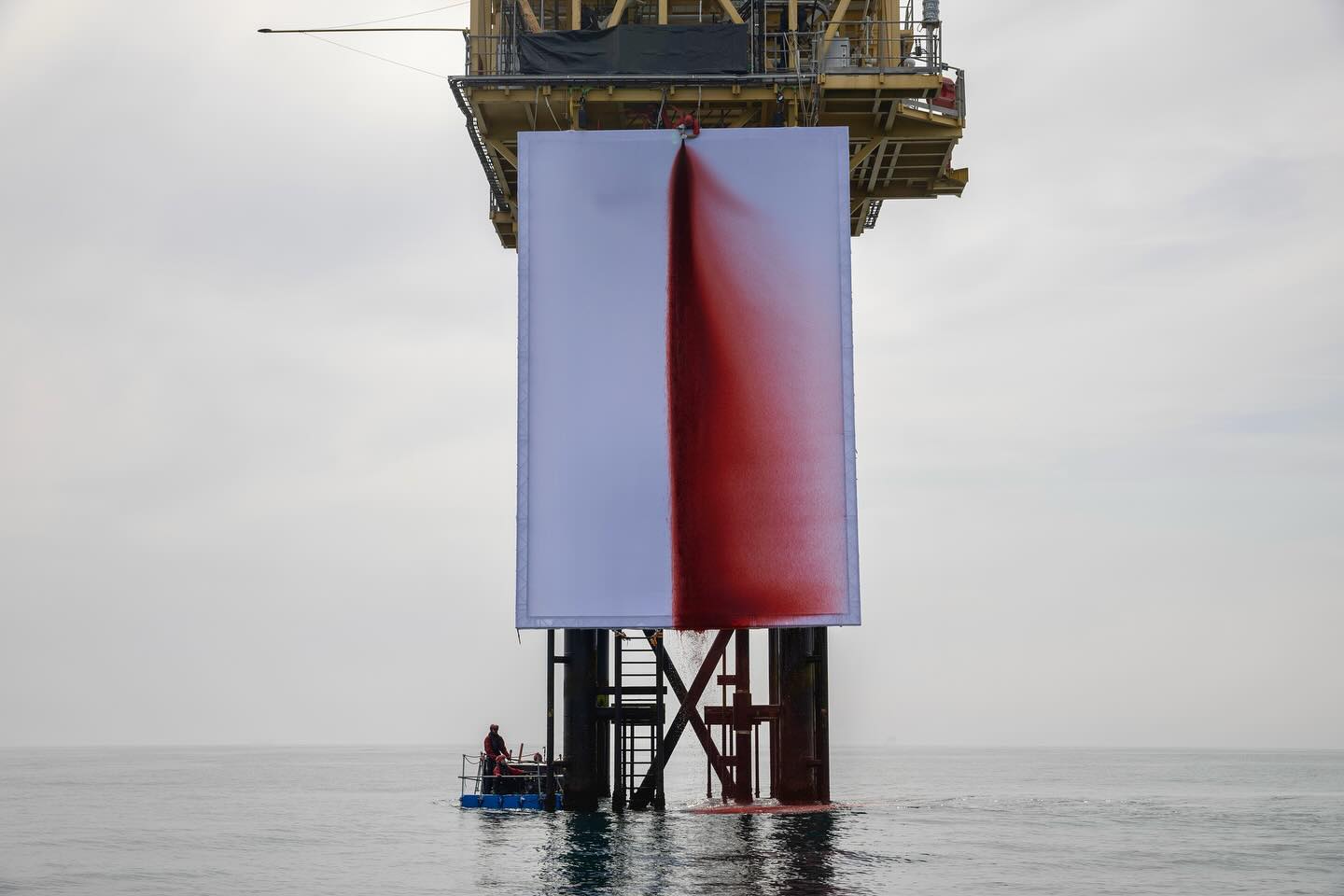 Greenpeace activists installing an artwork called BUTCHERED on a Shell gas platform, depicting red liquid spilling down a large white banner into the sea.