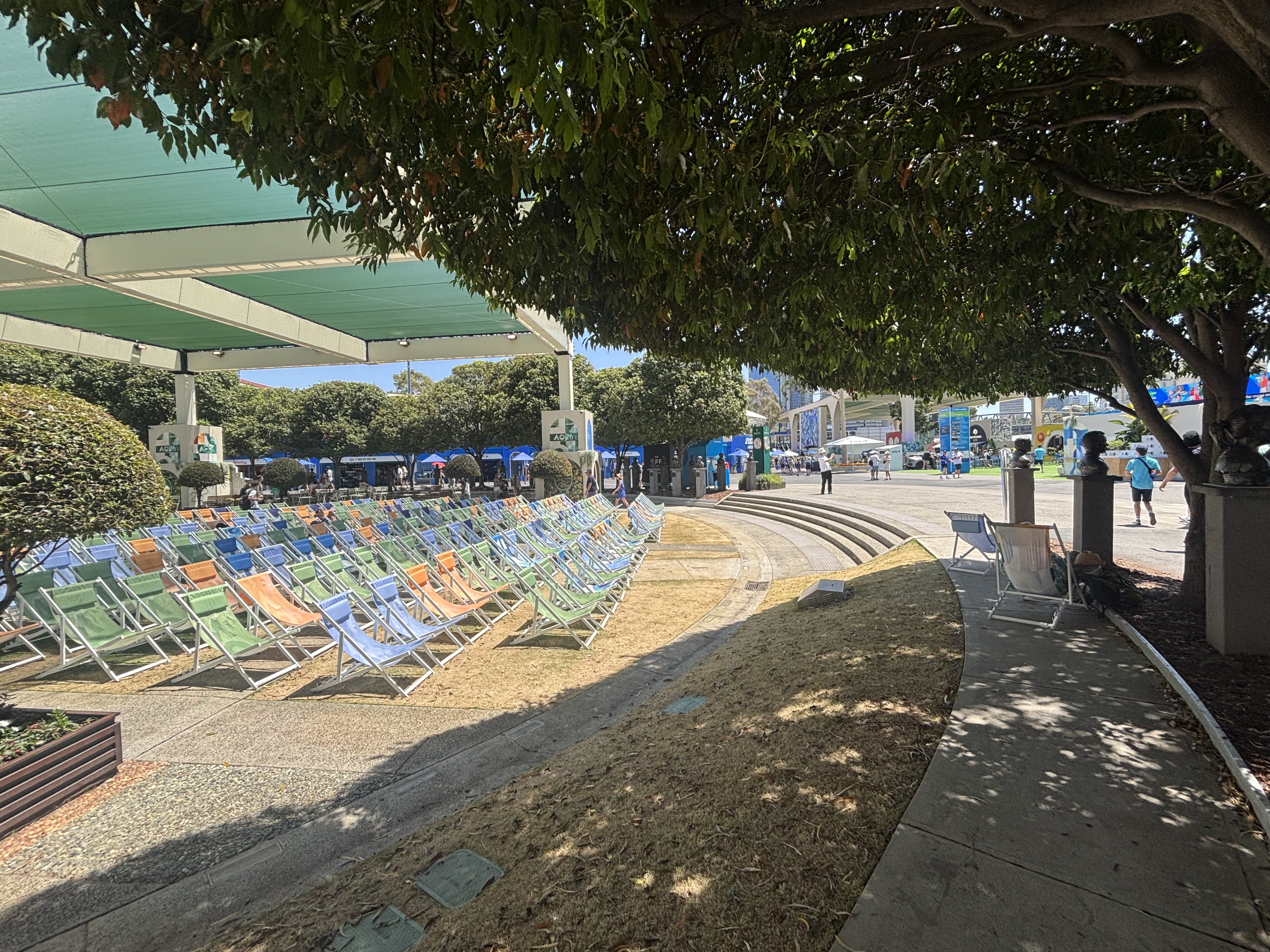 Colorful chairs under a teal awning and trees on a sunny day.