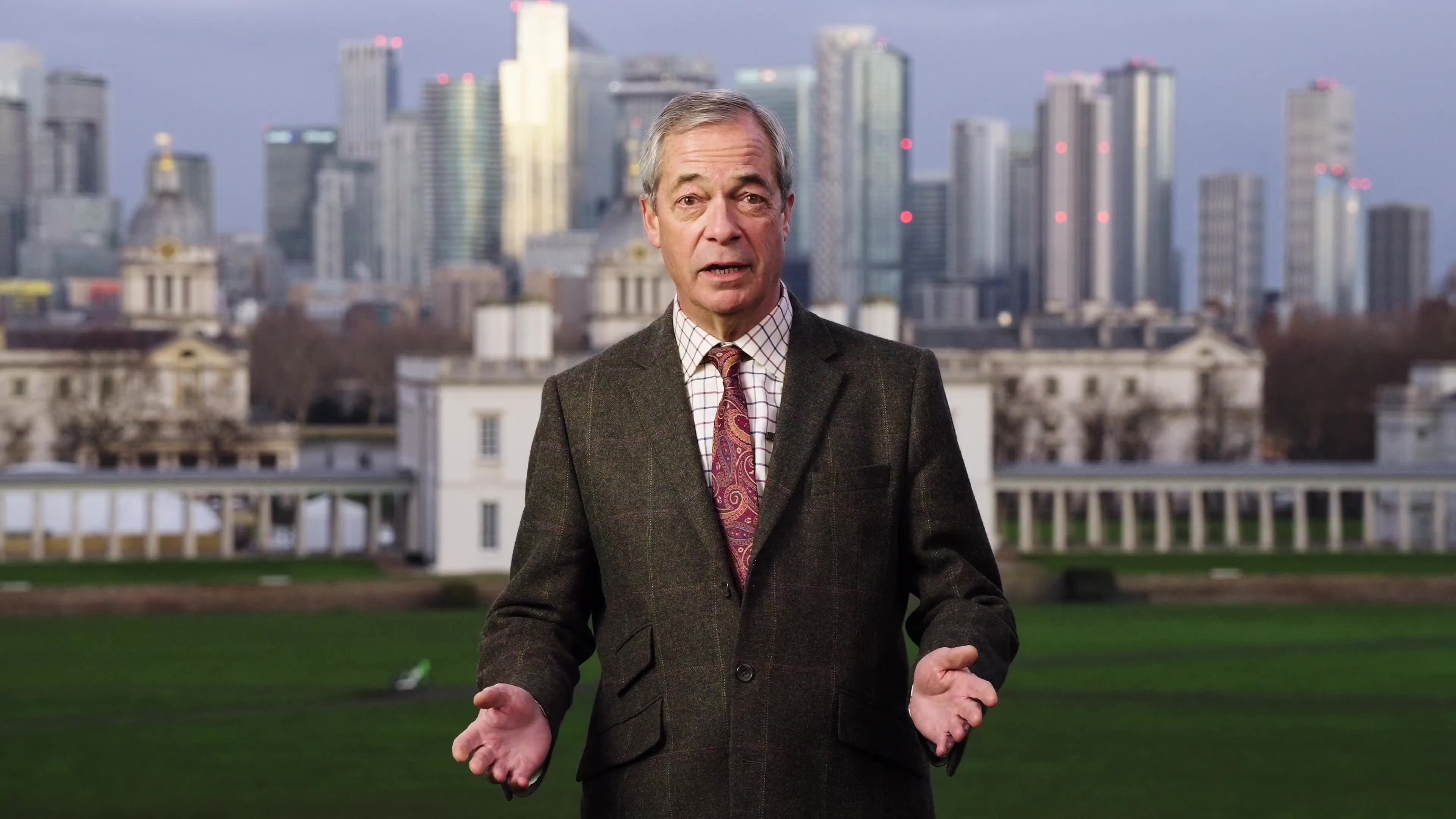 Nigel Farage in a suit and tie, gesturing with his hands, in front of a city skyline.