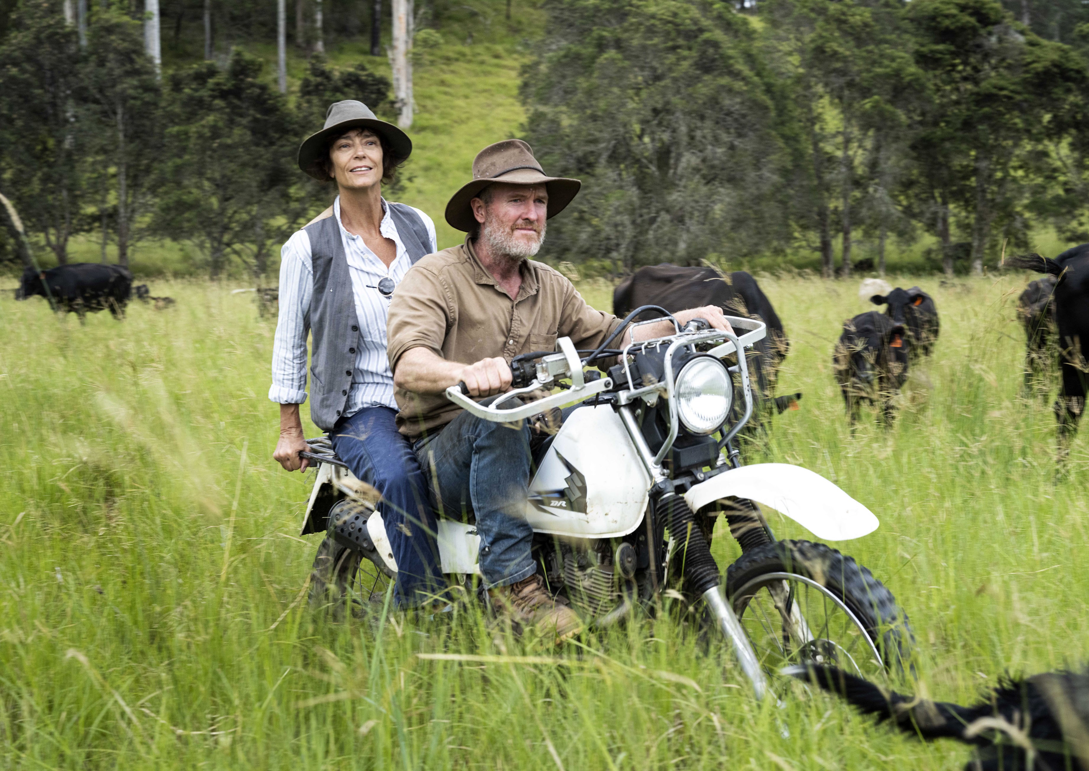 Rachel Ward and Mick Green (Jnr.) on a motorcycle in a field with cows.